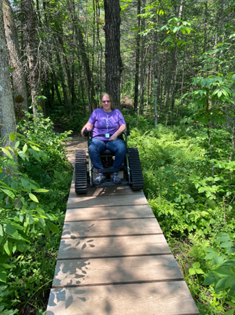 woman in outdoor wheelchair on narrow wooden path over marsh